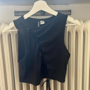 Svart ribbad linnetopp från Bershka - En svart ribbad linnetopp från hm med snörning framtill. Toppen är ärmlös och har en tight passform.