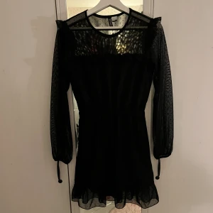 Volangklänning i mesh  - En svart kort prickig långärmad klänning i mesh med volang över axlarna, framtill och nedtill samt resår i midjan och vid ärmslut från H&M i strl XS!💓 