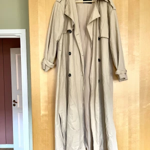 Den perfekt långa trenchcoaten - Lång trenchcoat med knappar på båda sidor i 100 % bomull från märket Y.A.S. Midjeband saknas! Storlek M, men skulle säga att den känns mer som en L då den är lite oversized.