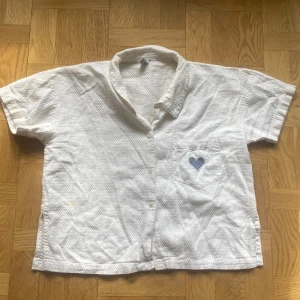 Söt vintage croppad skjorta  - Super söt kortare skjorta med ett broderat blått hjärta på bröstfickan 💙. Vintage från Hennes och Mauritz 