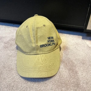 Keps - Beige keps med mörkblå/svart text. 