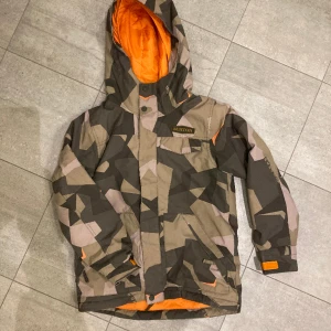 Vinterjacka Burton, 10-12 år - Ytterplagg, stl. 146/152 (10-12 år), Unisex Vinterjacka från Burton. Grön Vinterjacka från Burton. Grön Vinterjacka från Burton. Grön camouflage. Fint skick. Storlek junior M. 250 kr