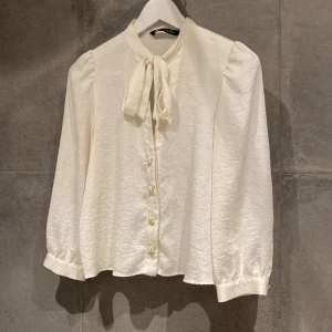 Silkig knytblus från Zara - Silkig knytblus från Zara. Fina detaljer med puffiga axlar och pärlknappar både fram och på ärmen.   Modellen är något croppad.