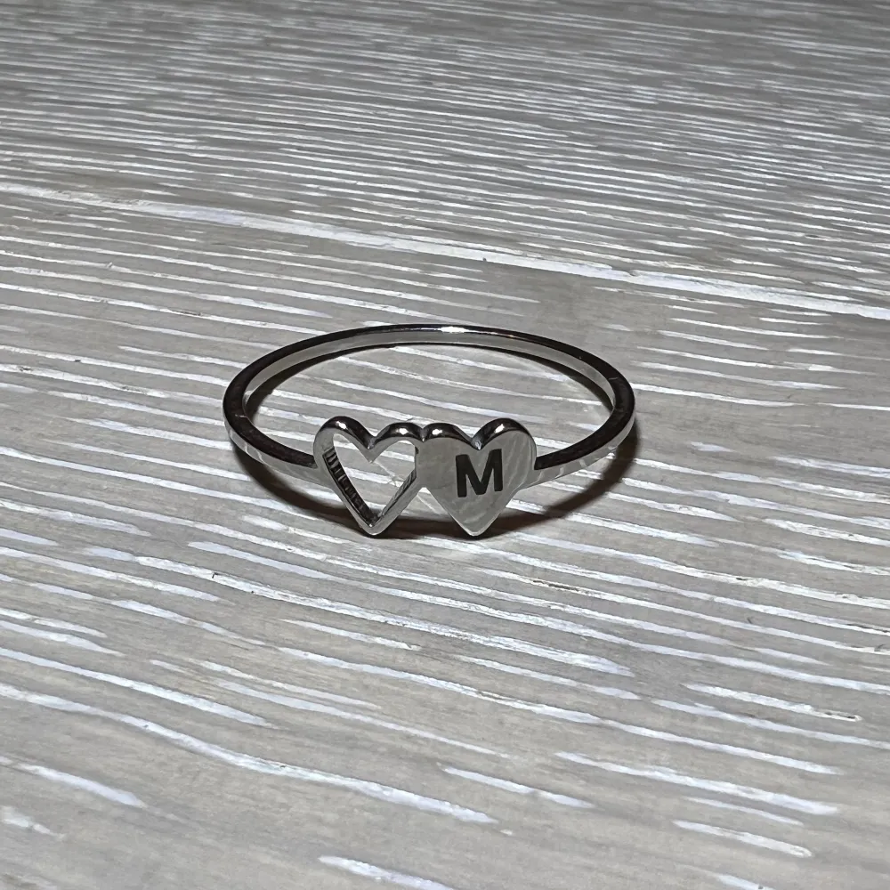 Väldigt fin, elegant ring i silverfärg. Den har två hjärtan som motiv, ett ”ihåligt” och ett med bokstaven M på!. Accessoarer.