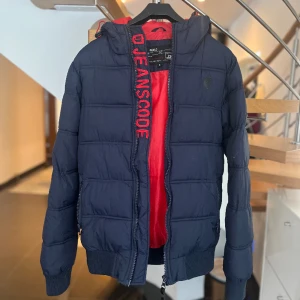 Jacka för män  - En fin jacka i storlek S som är i väldigt bra skick. Färgen på jackan är marinblå med röda detaljer vid insidan. 