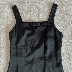 InWear svart elegant figursydd klänning med rosett - Otroligt stilig och elegant klänning från InWear med en liten gullig rosett vid bysten. Den har en sluts i mitten av klänningen baktill som inte är uppsprättad. Aldrig använd. Ny med snöre kvar. Har råkat få deofläckar som lätt går bort med handduk.