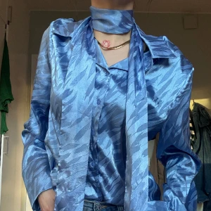 Satin blus med scarf - Blå satinblus med medföljande scarf detalj från NA-KD (scarfen kommer separat så man kan välja om man vill använda den eller inte) toppenskick endast använd ett fåtal gånger i storlek S
