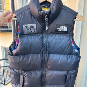 The North Face Flag Puffer Vest, fits size Small - Skön pufferväst från North Face, i väldigt gott skick då den endast använts ett fåtal gånger för några år sen. Cool flagg-print inuti och även i svart camouflage på utsidan. Boys size Large, passar herrstorlek Small. Kan mötas i Sthlm!