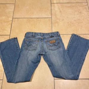 Lågmidjade jeans - Säljer ett par lågmidjade vintage bootcut jeans från wrangler så tyvärr har blivit för små för mig. Jättebra skick och en fin blå färg. I jeansen står det storlek w26 och L32 Midjemått:72 cm Innerbensläng:79cm 💕