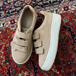 Sandro Paris skor - Säljer ett par beigea sneakers från Sandro Paris i storlek 36. Begagnat skick, finns viss tecken på användning. Finns tyvärr ingen medföljande kartong. Material: mocka  Kan hämtas upp på Östermalm alt postas! 