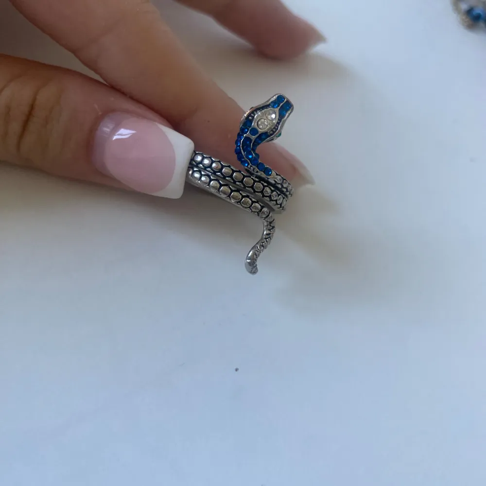 En unik ormformad ring i silver med blå detaljer. Ringen är designad för att slingra sig runt fingret och har en realistisk ormskinnsstruktur.. Accessoarer.