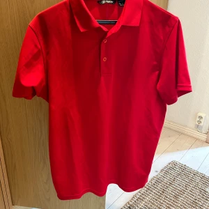 Röd pikétröja från Abacus - snygg golf piké! En röd pikétröja från Abacus med korta ärmar och en klassisk krage. Tröjan har en knappslå med tre knappar framtill.