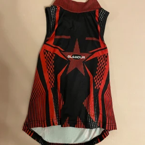 Svart och röd ärmlös topp från Glamour - En svart och röd ärmlös topp med ett stjärnmönster och geometriska detaljer. Toppen har en hög krage och är dekorerad med vita prickar på sidorna. Skriv gärna om ni har frågor 💕💕