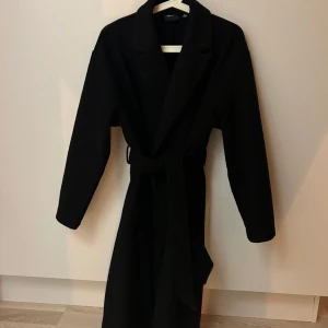 Svart kappa - Svart kappa med skärp.  Ok skick, lite nopprig vid kragen (går att ta bort)  