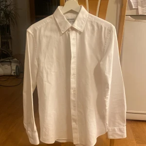 Oxfordskjorta Tiger Of Sweden  - Vit slim fit oxfordskjorta i strålande skick. Inga defekter förekommer. Rutig textur (se bild 2)  Ärmlängd: 63 cm Axel-axel: 45 cm midja: 95 cm Längd (rygg): 74 cm