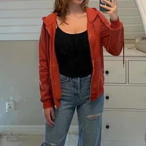 Hoodie med dragkedja - Fin hoodie med dragkedja. Färgen är orangebrun eller rostbrun, ser i verkligheten ut som på första och andra bilden. Jättebra skick, använd ca 2-3 gånger