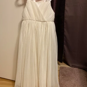 Glittrig klänning strl 134 - Så himla fin klänning! Säljes i fint skick.  Den enda defekten är en rosett jag inte kan hitta här hemma. Som kan knäppas fast på ryggen. Min dotter har däremot använt den utan denna rosett. Katt finns i hemmet (allergivänlig ras).