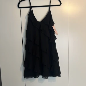 Svart volangkläning (oanvänd) - En helt oanvänd volangkläning från Nelly, den är tuvär förliten för mig och har derför aldrig anvends, lappen sitter fortfarande på och den är i nyskick då den aldrig använts❤️