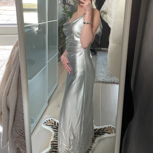 Silvrig långklänning😻 - Säljer denna fantastiska klänningen i ”silkes” material, då jag inte gillar hur den sitter på mig. Den har en slits vid benet och justerbara band. Bara använd en gång:) Nypris 700kr