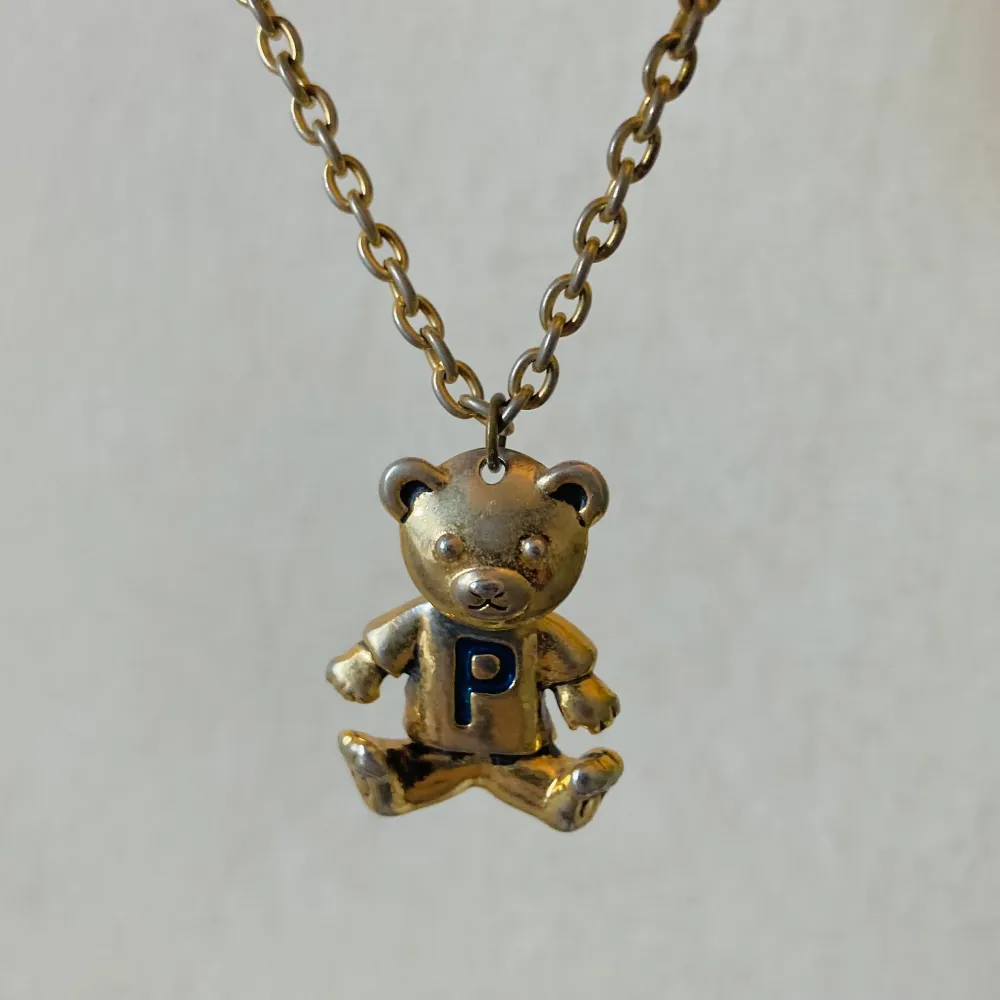 Vintage halsband från 90-talet. Okänd metall med guldig-plättering som skavits av med åren. Huvudet på nallen är rörligt.. Asusteet.