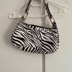 Zebramönstrad Axelväska - En jättefin axelväska perfekt till sommaren, väskan är använd Max 3 gånger så är i super bra skick. Väskan kommer från Nelly.