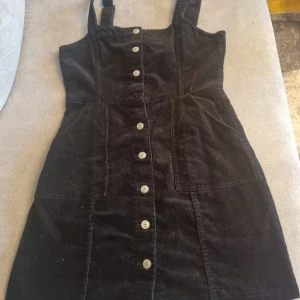 H&M Hängselklänning  - En Svart Manchester Hängselklänning I stl 38 (EUR), med knappar/knäppning hela vägen. Så himla fin klänning som ser väldigt bra ut med en T-shirt eller Långärmad under.  Klänningen är köpt från H&M för 299kr. Använd engång. Skicket är som på bild. 🤗💞