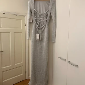 Stickad SILVRIG  klänning med öppen rygg - strlk S - Aldrig använd klänning med prislappen kvar.  Stickad i skincity material med öppen rygg som går att justera!   Storlek S - jag är 165cm och den går hela vägen ner till fötterna.  Hämtas i Stockholm city