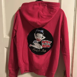 Tjocktröja med dragkedja  - Rosa tjocktröja med dragkedja med Betty Boop tryck på ryggen och text på bröstet och ena armen. Lite trådning på snörena som man kan se på bild 2 annars bra skick💗 Jag anser att storleken kan passa S-L beroende på hur man vill ha passformen.