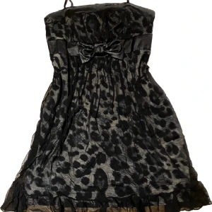 Söt klänning  - Super söt klänning med vittsvart leopardmönster med mech tyg ovan på, under bysten är den en svart rosett  med band ut på sidorna. Klänningen är  ca 75 cm lång och är rätt så stretching.🎀
