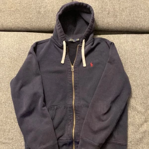 Ralph Lauren zip up - Säljer denna fina polo tröja i mörkblå färg, bra skick. Det ända vad jag vet av tröjan är lilla märket på botten av armen som syns på sista bilden. Storleken är L men är väldigt liten i passformen och skulle då säga att den passar mer M