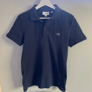 Lacoste Piké  - Riktigt snygg mörkblå Lacoste piké i riktigt bra nyskick:(9,5/10). Den är sparsamt använd och har inga tecken på användning och nypris är ca 1300 kr. Snygg nu till vår och sommar. Passar storlek S.  Skriv för frågor! //Carl