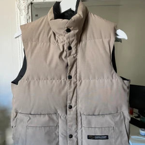 Canada goose väst - Hej, jag säljer en riktigt snygg Canada goose väst i en äldre modell, färgen är beige och den är använd men i snyggt skick, storlek XS men passar upp till M. Skriv om ni har några funderingar😁