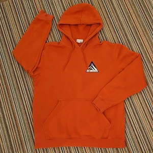 Hoddie - En orange hoodie med en logga på ena bröstet. Ingen design på ryggen.