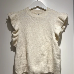 Stickad topp - Söt stickad vit/ljus begie topp med volang ärmar. I en t-shirt modell. 