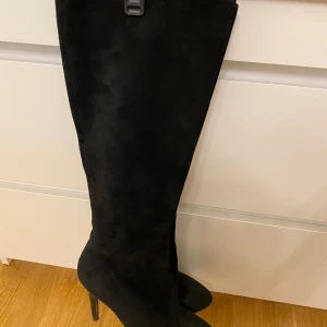 Knähöga kaxiga stövlar med stilettklackar. Y2K style. - Knähöga kaxiga stövlar med stilettklackar. Y2K style. I bra skick med några få tecken av användning. Stövlarna är bekväma och stabila. Gjorda av äkta suede, mocka. Sparsamt använda.  Nypris ca 3000 svenska kronor. UK. 