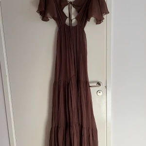 Långklänning med fina detaljer - Brun, superfin långklänning från Asos. Den är tyvärr lite ”hålig” längst ner i yttertyget då den fastnade i en taggbuske. Det är dock inget som syns när man bär klänningen. Storlek XS men har resor i ryggen och passar därför upp till M. Köpt för 899 