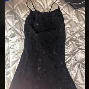 Svart klänning med blommigt mönster - Svart kort klänning med lite öppen rygg och korsade band. Blommigt svart, lite glansigt mönster.