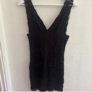 Kort och svart spetsklänning från RebeccaStella i strl M. Korsettliknande stängning i ryggen 