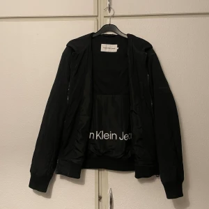 Calvin Klein Bomberjacka - Stil och Kvalitet!  - Ta din stil till nästa nivå med denna klassiska bomberjacka från Calvin Klein. Trots att den är begagnad, är den i utmärkt skick och nästan som ny. 