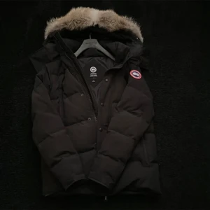 Canada Goosejacka - Svart dunjacka från Canada Goose. Två stora framfickor som stängs med dragkedja med två mindre fickor inuti med fleecefoder, en innerficka och avtagbar naturpäls på luvan. Jackan är i använt men bra skick,nypris ca 16 000