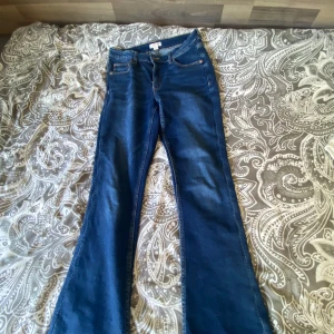 Blå jeansbyxor från Gina Tricot - Ett par blå jeansbyxor från Gina Tricot. Byxorna har en klassisk design med dragkedja och knapp framtill. De har en bootcut-stil som är något utsvängda vid benen.