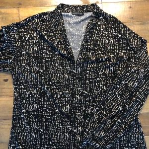 Svart och vit mönstrad klänning från Stockh LM - En elegant svart klänning med vitt mönster från Stockh LM. Klänningen har långa ärmar och en v-ringad hals.