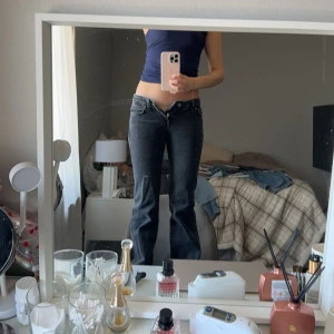 Svarta jeansbyxor - Ett par svarta jeansbyxor med låg midja och bootcut-stil. Byxorna har fickor både fram och bak samt knappar och dragkedja. Y2k stil