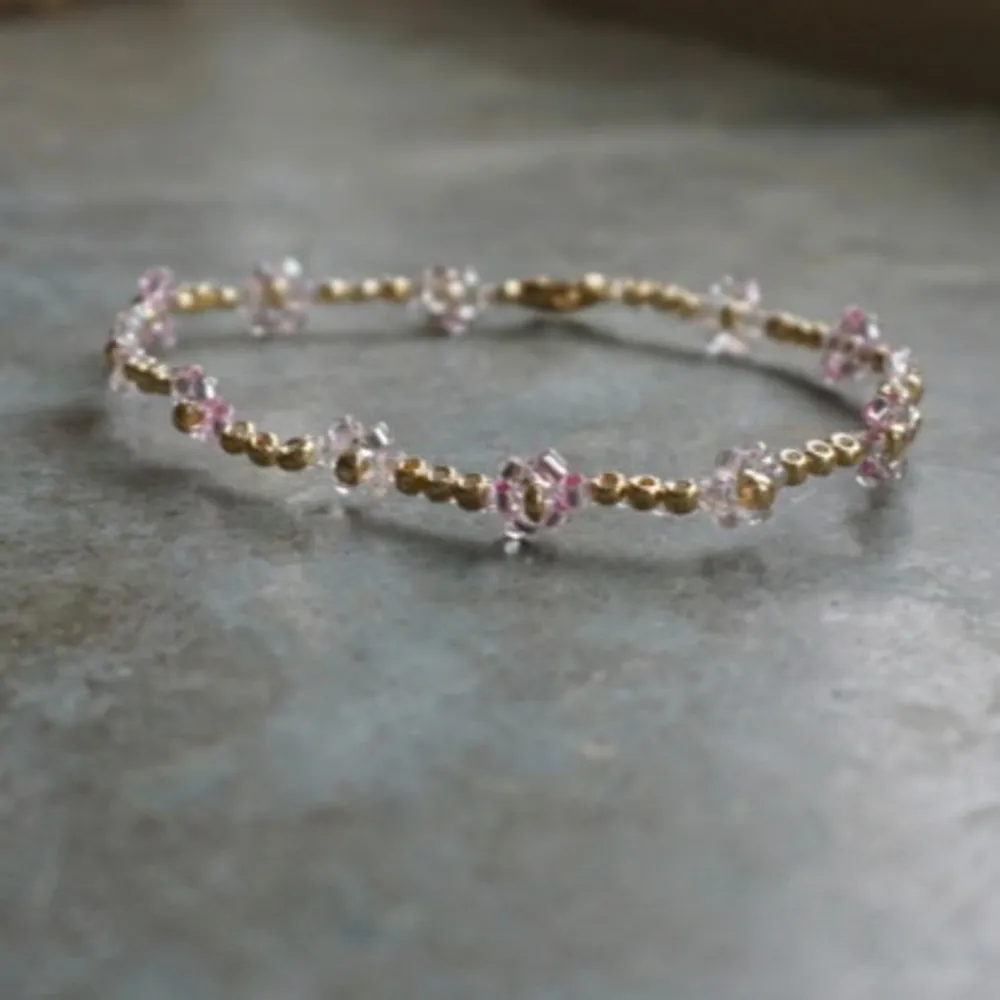 Ett elegant guldfärgat armband dekorerat med små rosa pärlor. Armbandet har en tunn design med pärlor placerade med jämna mellanrum, vilket ger det en delikat och stilren look.. Accessoarer.