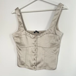 Korsettopp - Topp från ginatricot i strl xs. Toppen är i beige satin och knäpps med knapparna! Använd en gång men det oanvänd ut