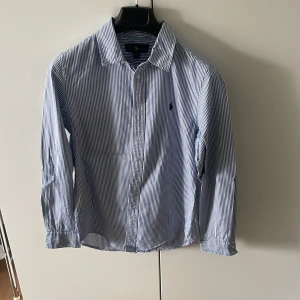 Blå/vit randig Ralph Lauren skjorta - Fin blå/vit randig Ralph lauren skjorta.  Säljer då den inte passar längre. Storleken är 16y vilket motsvarar XS/S