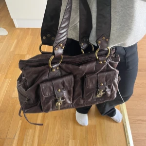 Väska  - As snygg brun väska med metall detaljer. Vet tyvärr inte märke på den då den är köpt utomlands!! Hör av dig för fler bilder<3 Pris går att diskutera vid snabb affär. (Ena metall kroken på framsidan gör ej att fästa)