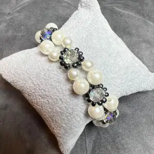 Vackert pärlarmband med vita pärlor och små svarta som omringar diamantlika pärlor och med ett silvrigt spänne. Justerbar passform mellan 19-24 cm. 