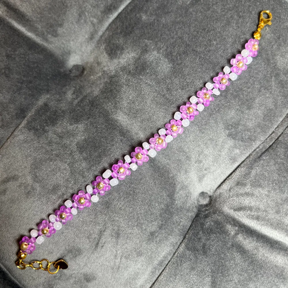 Egentillverkat pärlarmband med vackra rosa blommor, vita och guldfärgade pärlor och guldigt spänne. Justerbar passform mellan 18-20 cm.. Accessoarer.