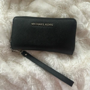 Michael Kors plånbok - Plånbok i skinn från Michael Kors. I fint skick, men bokstäverna är lite slitna, dock inget som syns om man inte kollar noga. Flera innerfack, mobilen får även plats. Mått: D: 2,5 cm x H 9 cm x B 18 cm.
